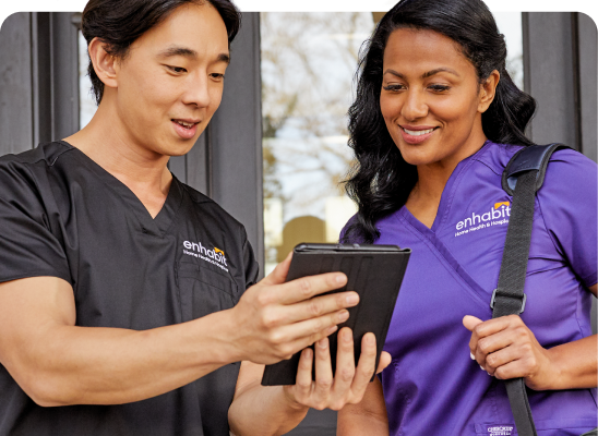 Male Enhabit clinician reviewing real-time patient information on handheld electronic tablet and discussing home-based care plan with female colleague
