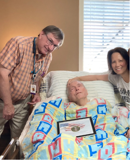 An Enhabit hospice chaplain poses with a hospice patient and the patient's wife. The veteran hospice patient is smiling with his certificate of recognition for his military service and commemorative pin.