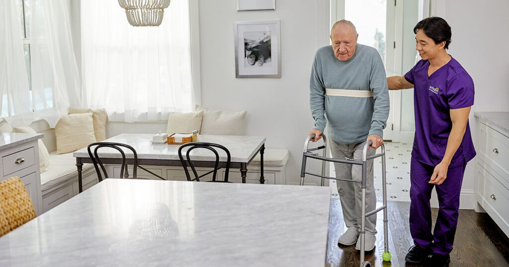 A home health occupational therapist helps a patient walk into their kitchen