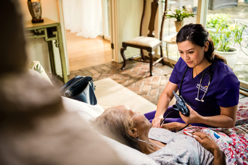 A hospice nurse sits with a patient at the bedside.