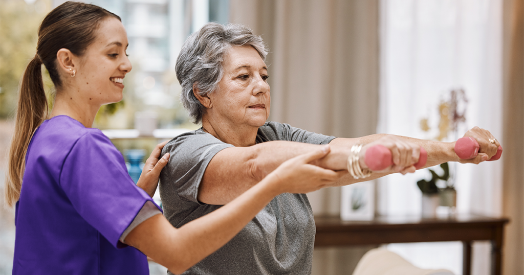 At Enhabit, our home health physical therapists serve as a critical component of the care journey. This home health physical therapist is helping an older woman lift weights out straight in front of her.