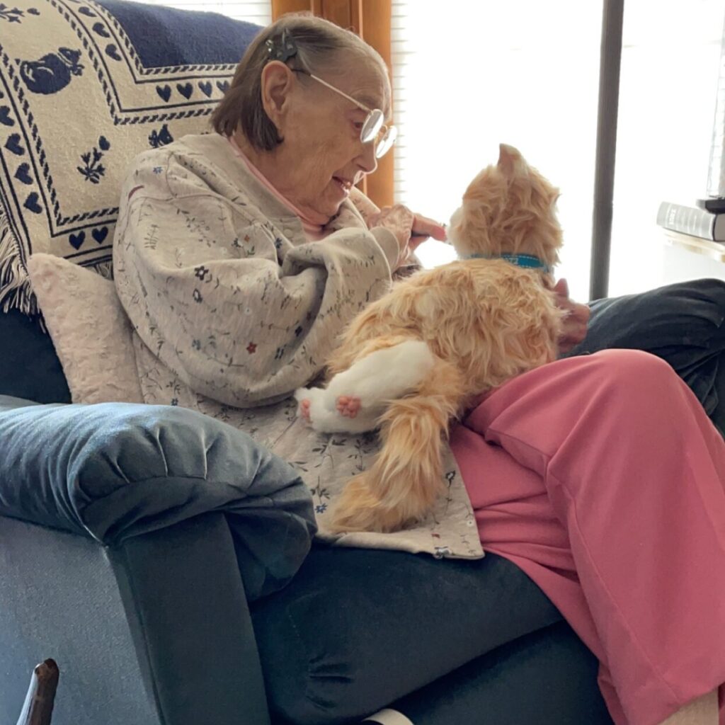Hospice patient Martha plays with her AI therapy cat while sitting on a blue recliner