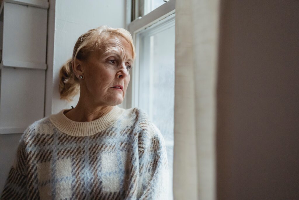 This image depicts an older woman longingly staring out the window, representing seasonal affective disorder.