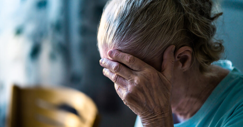 An older woman holds her head in her hand, signifying the effects that grief can have on the brain