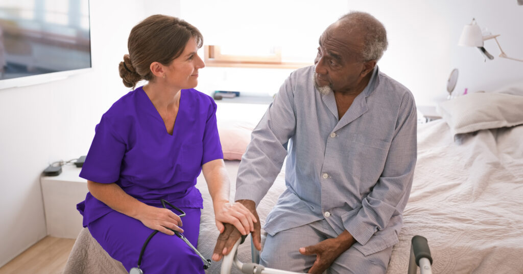 A clinician wearing purple scrubs talks to an older patient with a walker about the Care Connections Program