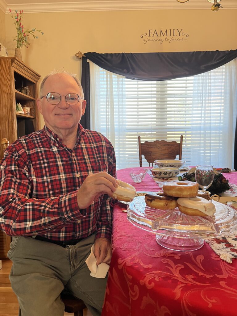 Enhabit patient John's stroke recovery goal was to eat a donut again with his right hand. He is pictured grabbing a donut off of a platter and smiling