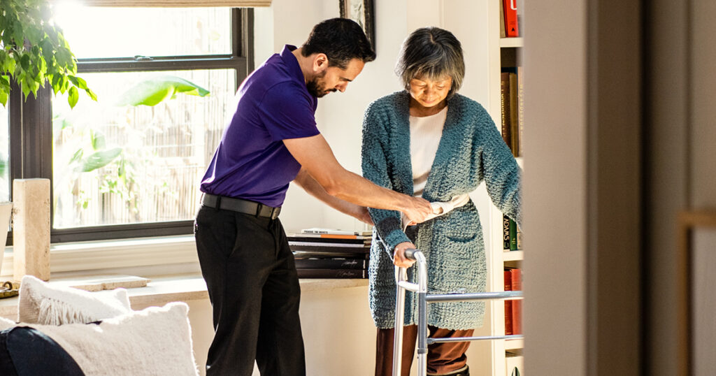 An Enhabit clinician helps a homebound patient move around her home using a walker and a gait belt