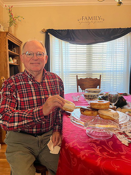 Enhabit patient John's stroke recovery goal was to eat a donut again with his right hand. He is pictured grabbing a donut off of a platter and smiling